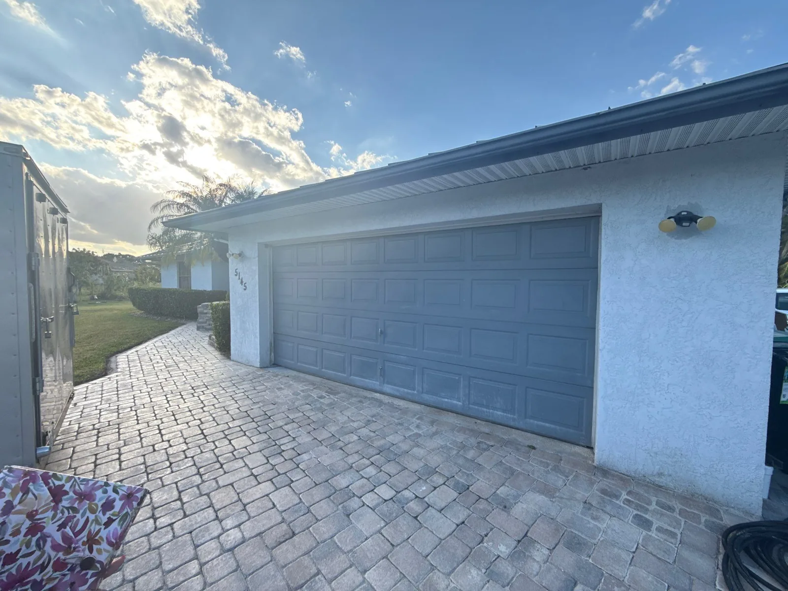 Exterior Painting in White City, Florida. Grey painted two-car garage door and stucco wall with paver driveway, shot in late afternoon light.