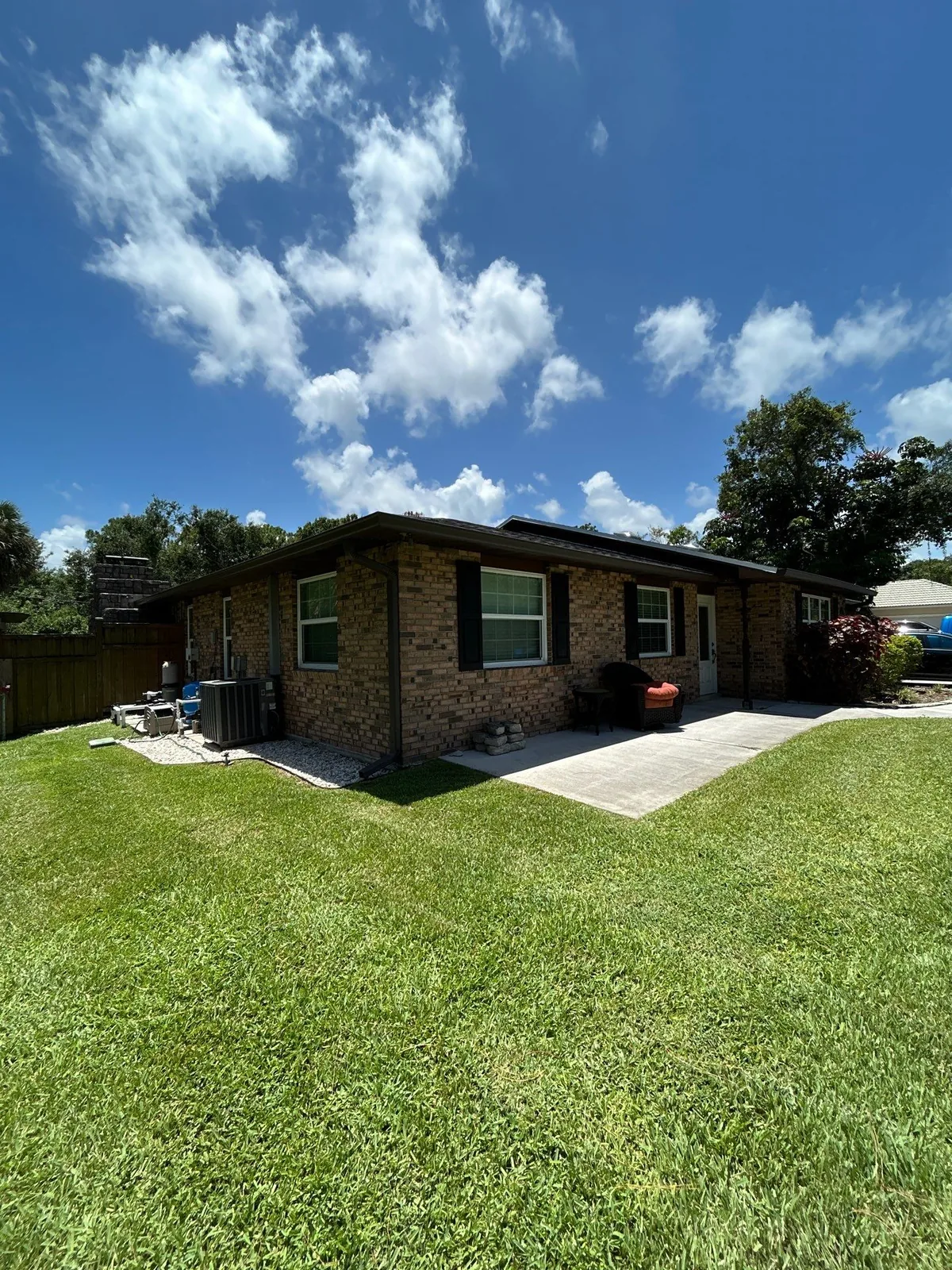 Exterior Painting in White City, Florida. Single-storey brick house exterior with dark painted fascia, soffit and window trim, green lawn and blue sky.