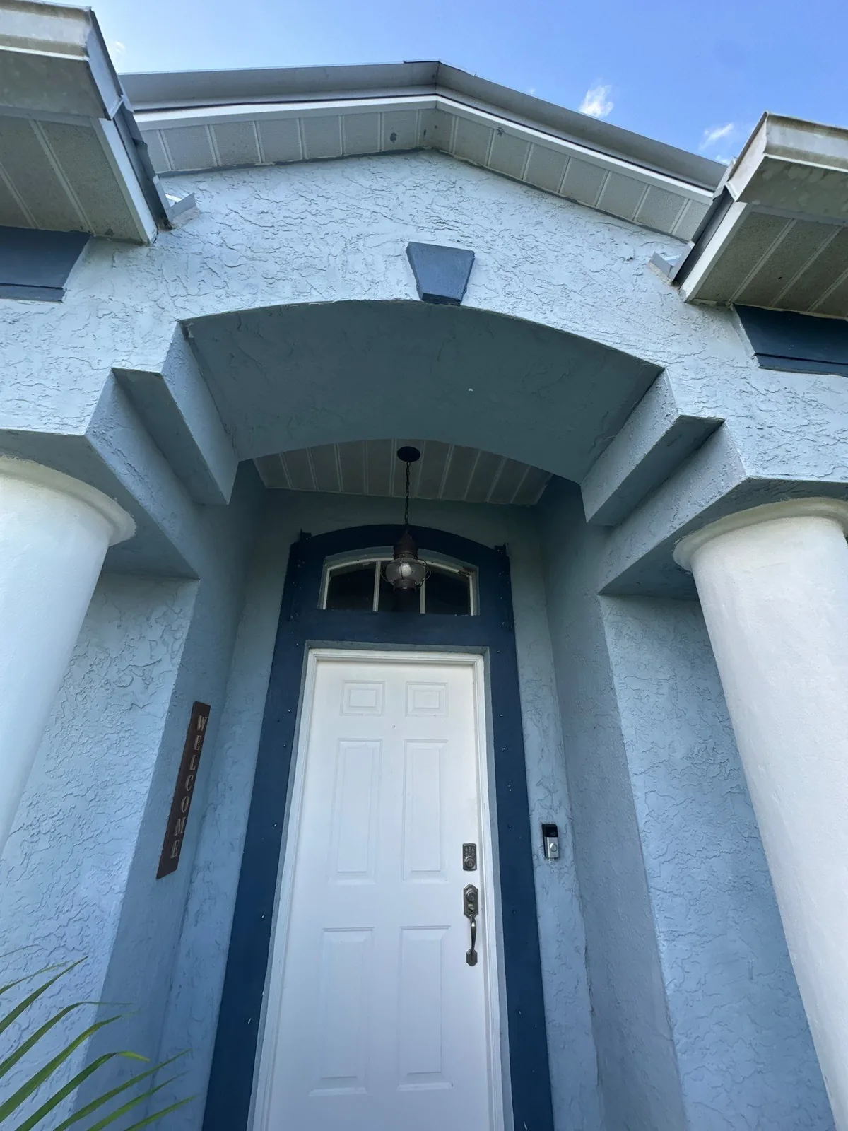 Exterior Painting in White City, Florida. Arched front entry of a house with blue-grey stucco, darker blue door surround and a white panelled front door.