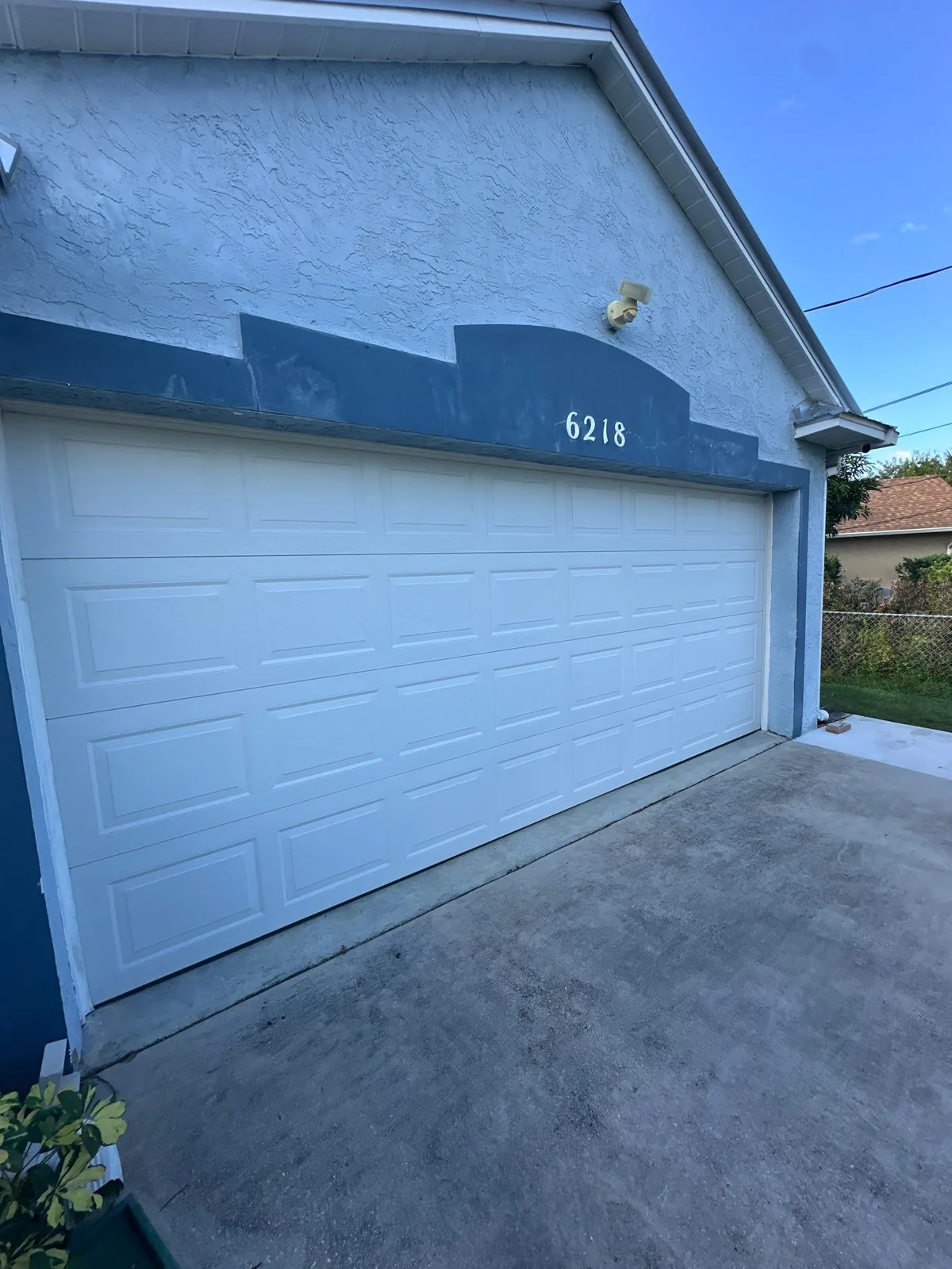 Exterior Painting in White City, Florida. Two-car garage with a white sectional door set into blue-grey stucco with darker blue trim and white house numbers.