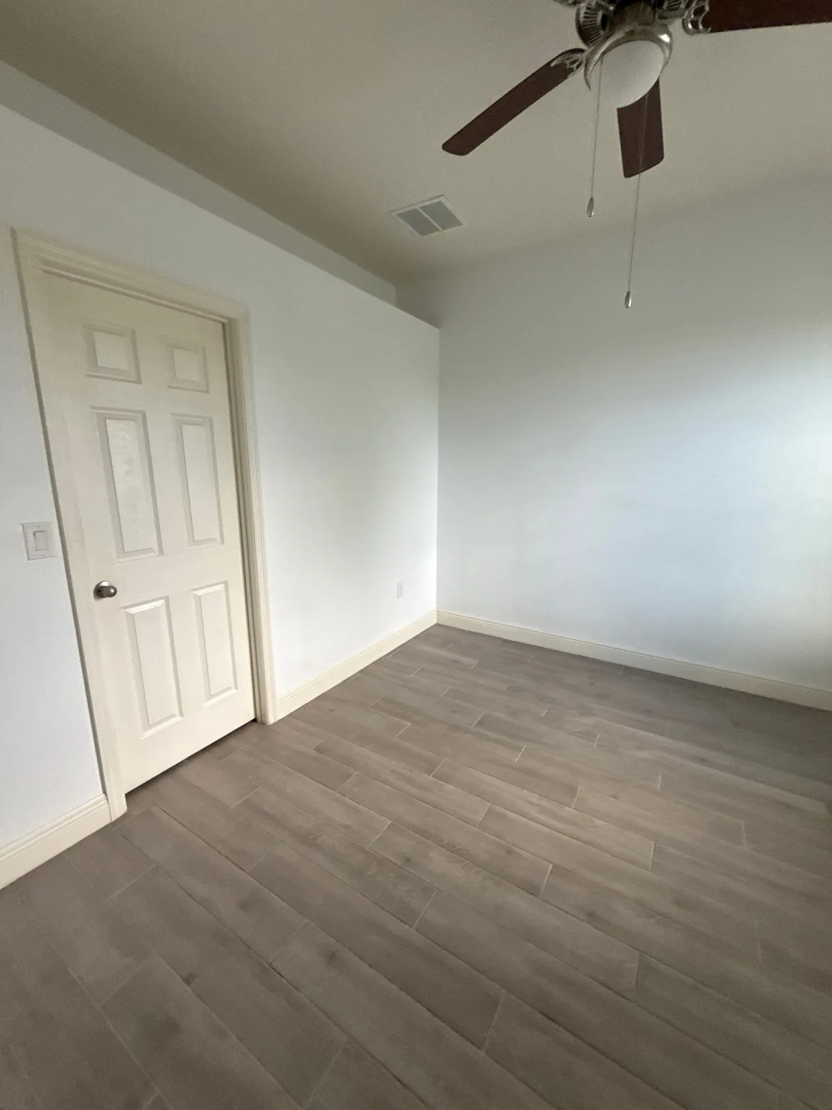 Interior Painting in Winter Beach, Florida. Empty bedroom with white walls, white six-panel door, wood-look plank floor and ceiling fan.