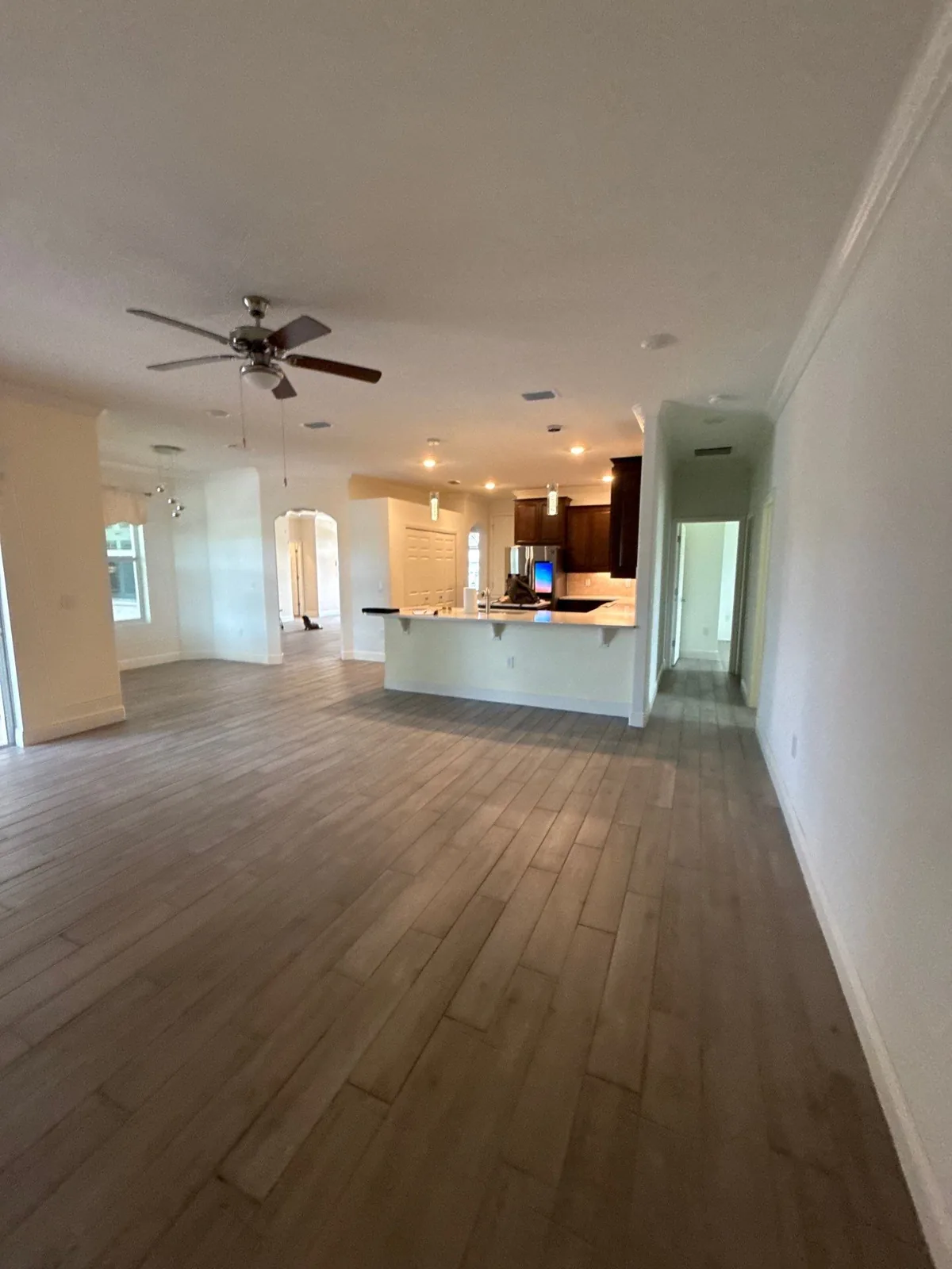 Interior Painting in Winter Beach, Florida. Empty open-plan living area with white walls, crown moulding, wood-look plank floor and a kitchen island beyond.