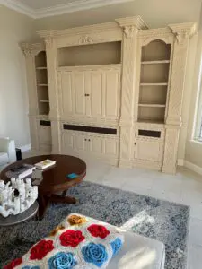 Traditional cream-colored ornate built-in entertainment center with fluted columns and crown molding in a living room with a round wooden coffee table.