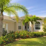 A sandy beige stucco home with a clay tile roof and palm trees showing exterior paint colors for a Florida home