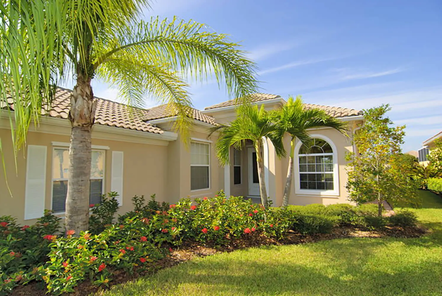A sandy beige stucco home with a clay tile roof and palm trees showing exterior paint colors for a Florida home