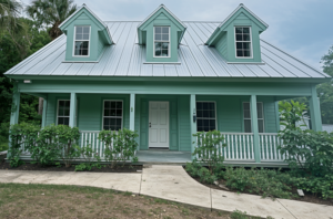 Mint green coastal cottage with three dormer windows, a silver standing seam metal roof, and a white front door.