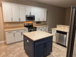 Modern kitchen featuring white perimeter cabinets, a navy blue center island, tan quartz countertops, and stainless steel appliances.