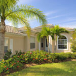 A sandy beige stucco home with a clay tile roof and palm trees showing exterior paint colors for a Florida home