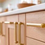 Close-up of natural wood kitchen cabinet drawers with gold hardware showing signs its time to refinish cabinets