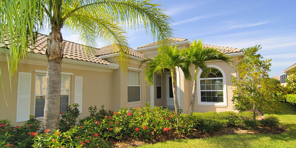 A sandy beige stucco home with a clay tile roof and palm trees showing exterior paint colors for a Florida home